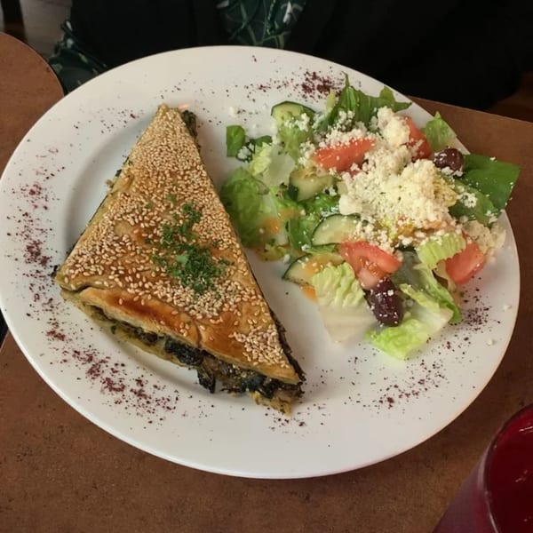 A triangular spanakopita with sesame seeds and a side Greek salad with feta cheese.
