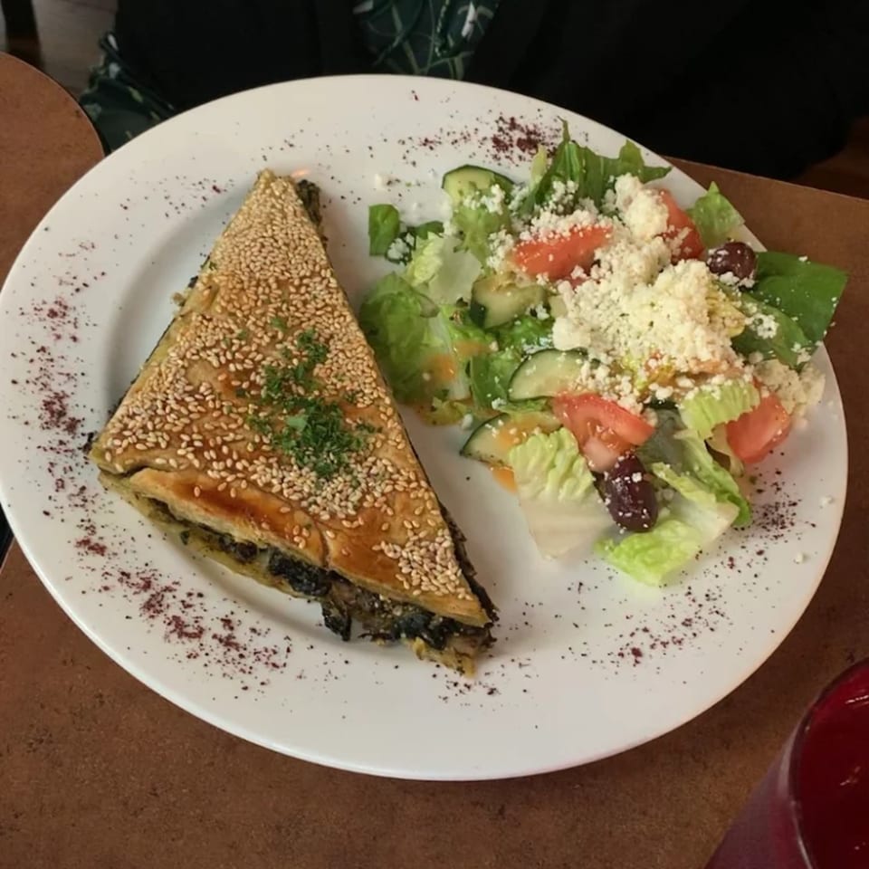 A triangular spanakopita with sesame seeds and a side Greek salad with feta cheese.