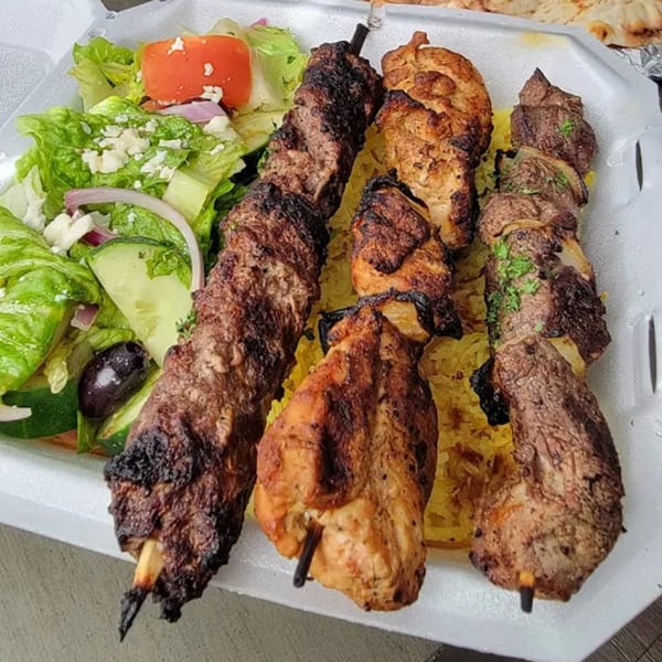 Three skewers of grilled meat, yellow rice, and a Greek salad with feta, olives, and tomatoes.