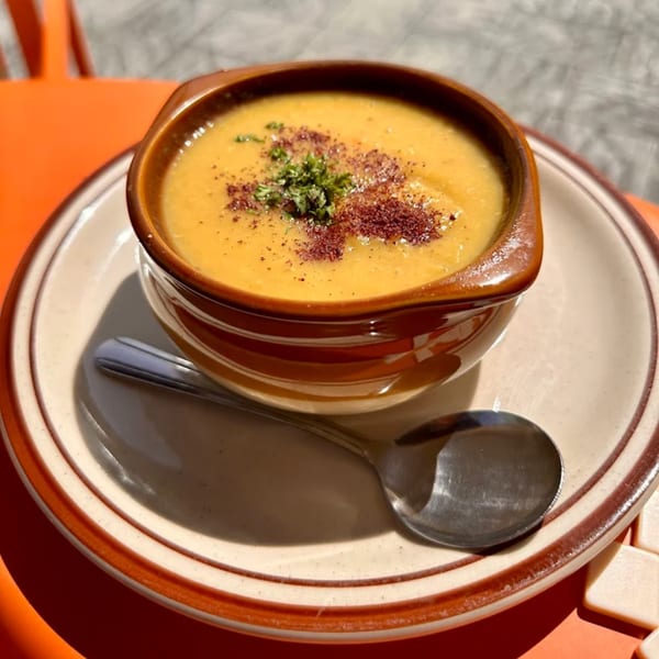 A bowl of Greek lentil soup, garnished with herbs and spices, on a plate with a spoon.