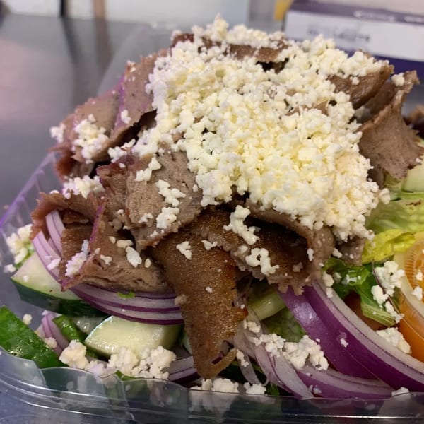 A close-up of a Greek gyro salad with meat, feta cheese, red onions, and cucumbers.
