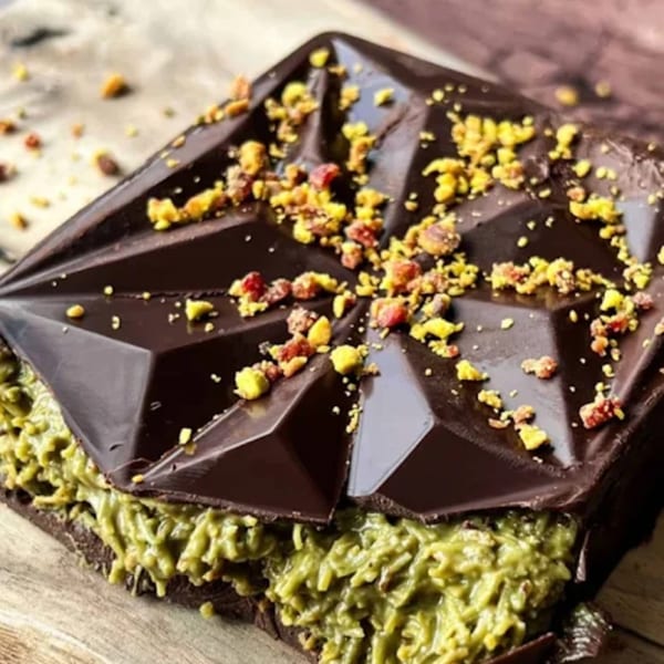 A geometric dark chocolate bar with a green pistachio filling and sprinkled with chopped pistachios.