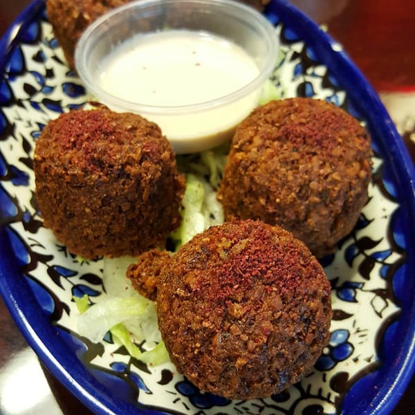 Three falafel balls with red spice on top, served with shredded lettuce and a side of white sauce.